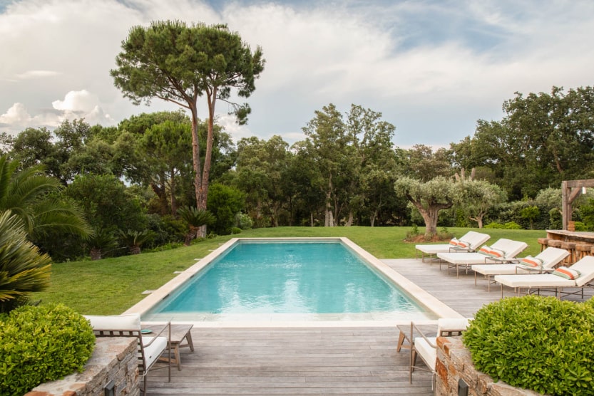 piscine-exterieure-entouree-de-transats-blancs-avec-des-coussins-beiges-et-orange-et-d-un-jardin-arbore