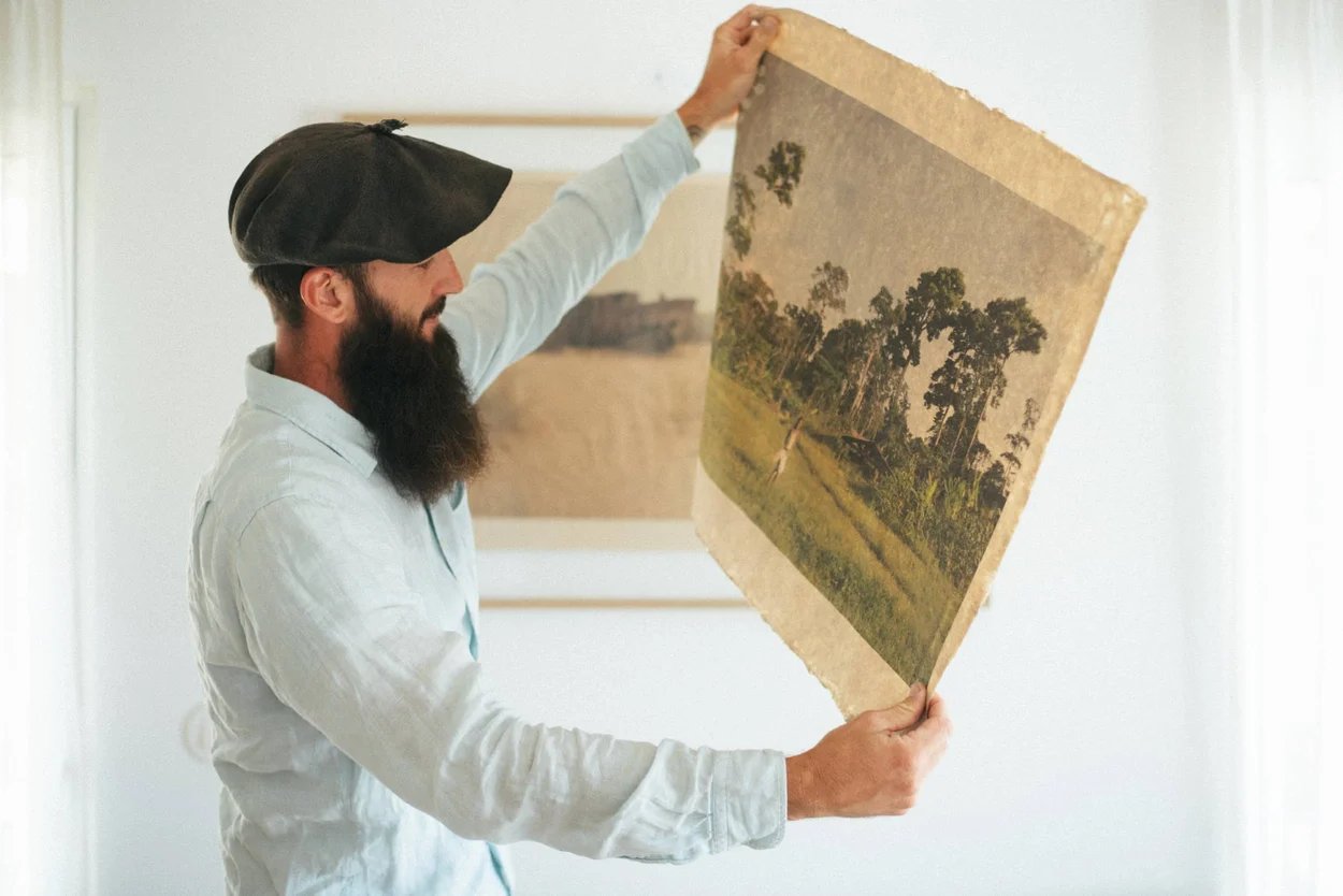 homme-brun-avec-une-chemise-et-un-beret-tiens-une-vieille-carte-avec-un-paysage-verdoyant-dans-les-mains-dans-une-piece-blanche