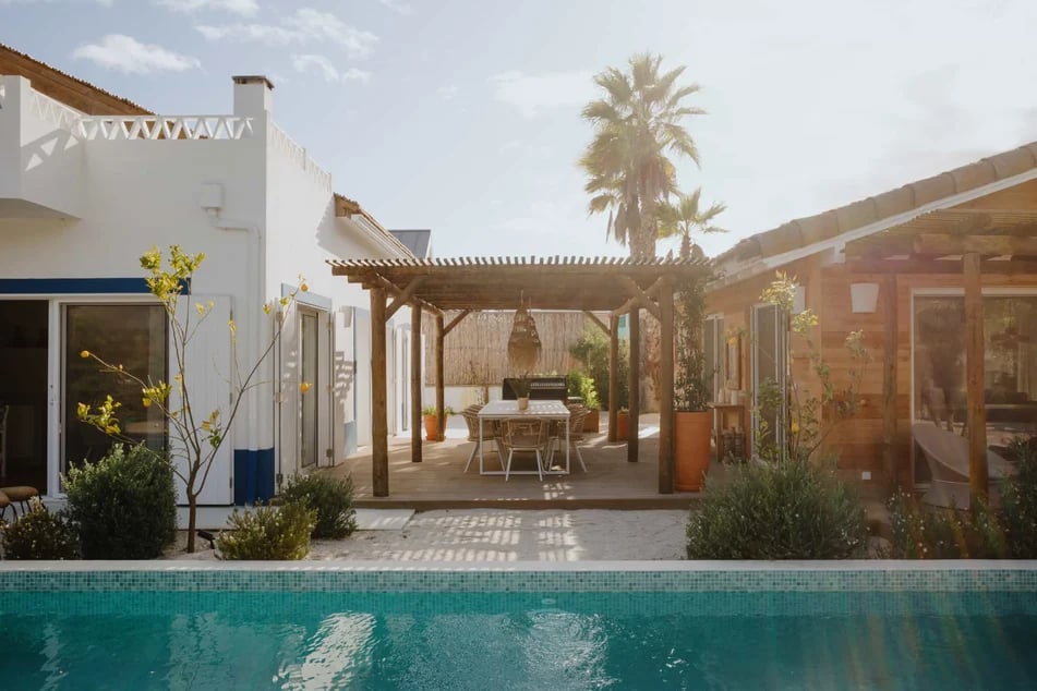 exterieur-d-une-maison-aux-facades-blanche-avec-une-pergola-en-bois-des-arbustes-et-une-piscine