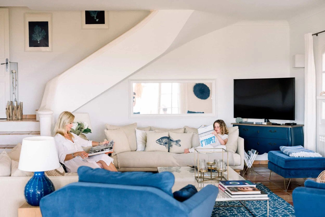 une-femme-blonde-et-une-petite-fille-lisent-des-magazines-assises-sur-un-canape-beige-dans-un-salon-avec-des-meubles-bleu-et-blancs