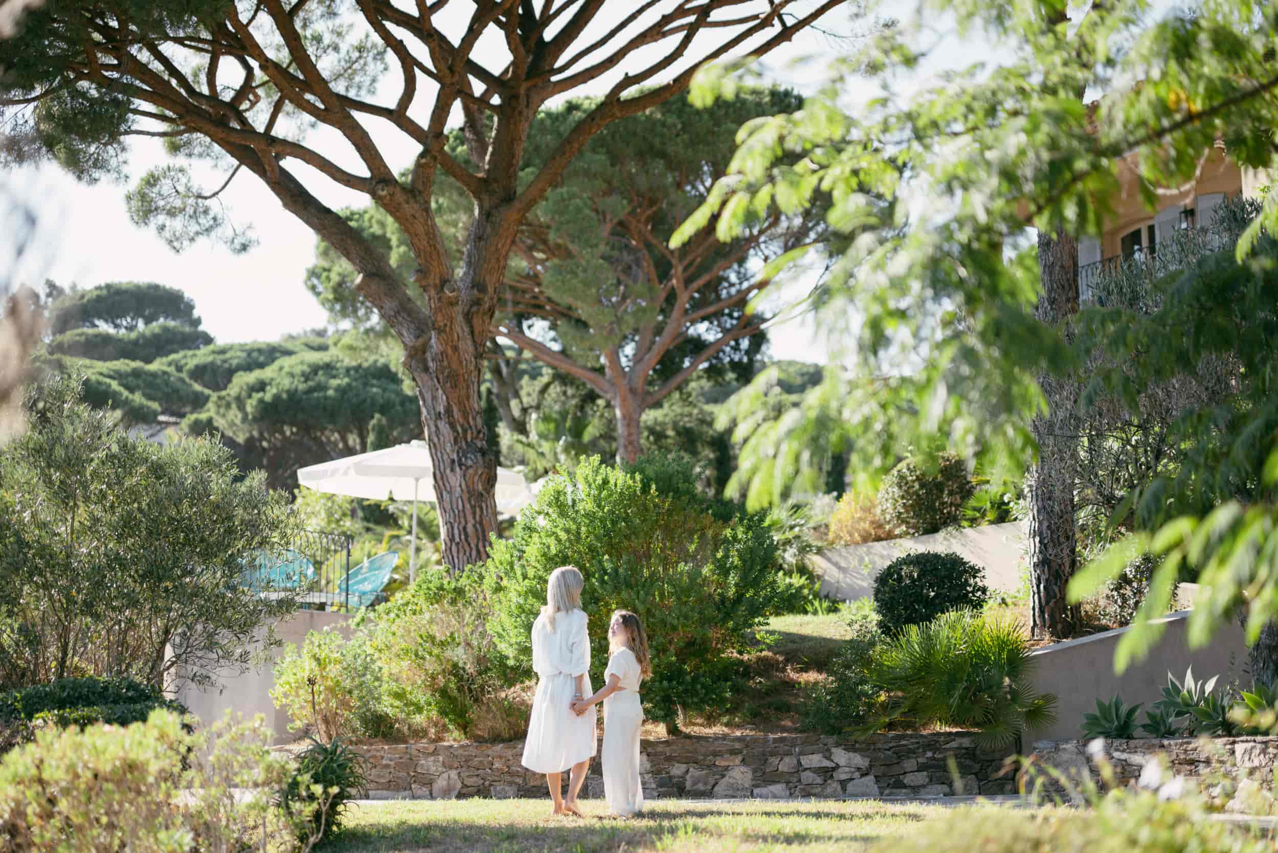 une-mere-et-sa-fille-se-tiennent-la-main-debout-dans-un-jardin-verdoyant-et-arbore-autour-d-une-villa
