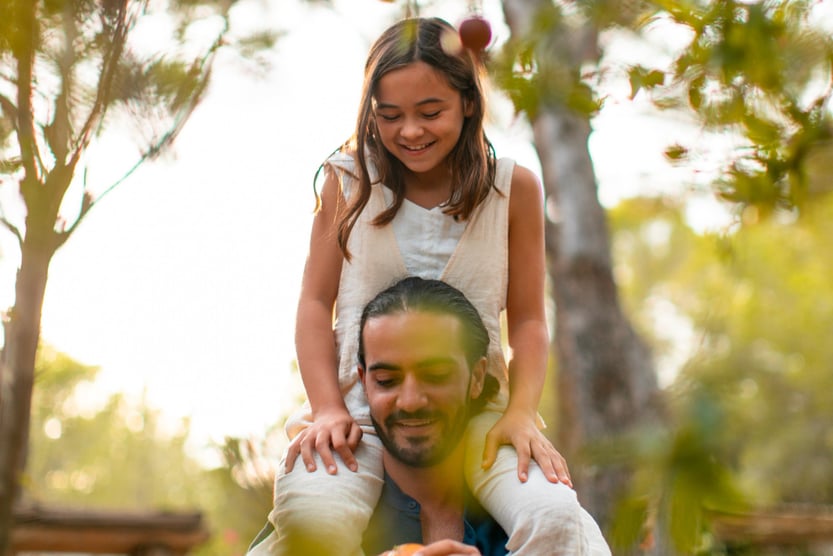 young girl picking fruit on her father's shoulders