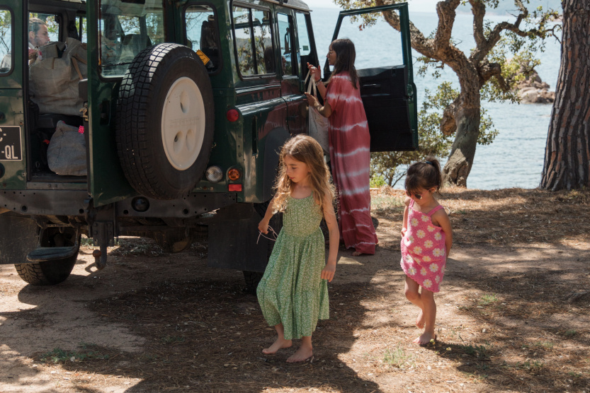 two children behind a jeep while the mother unpacks luggage from the vehicle