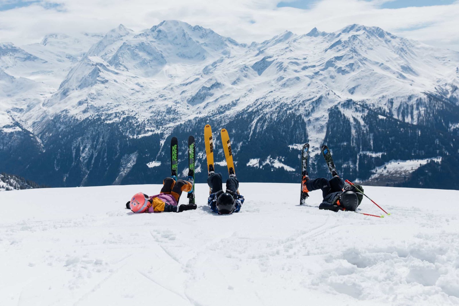 Trois enfants au repos dans la neige, skis plantés face aux sommets