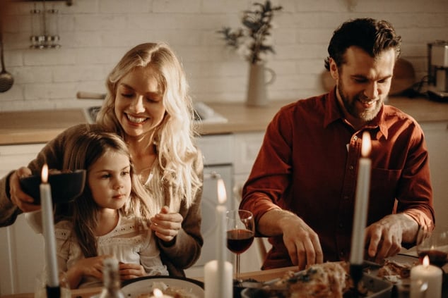 couple-brown-haired-man-and-blonde-woman-with-a-little-girl-sat-on-her-knee-at-a-table-with-food-bottles-of-wine