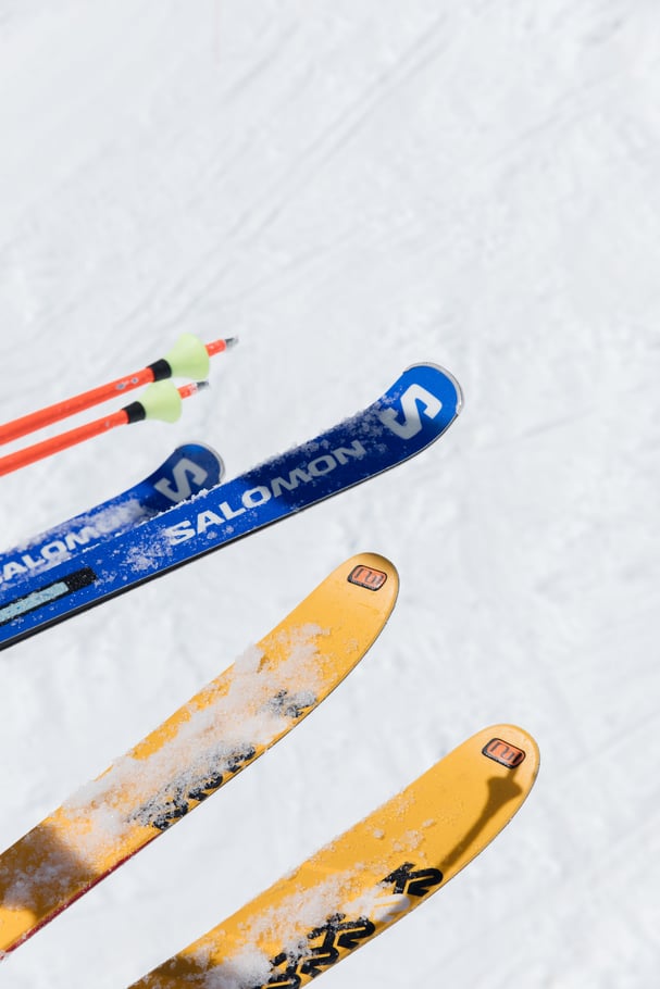 zoom-sur-deux-paires-de-ski-une-jaune-une-bleu-avec-des-batons-rouges-et-verts-sur-la-neige