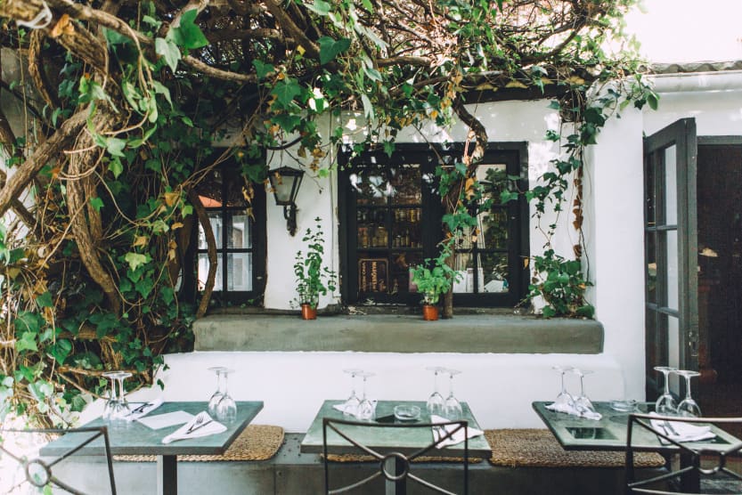 trois-tables-dressees-sur-une-terrasse-d-un-restaurant-typique-a-la-facade-blanche-entouree-par-les-branches-d-un-arbre