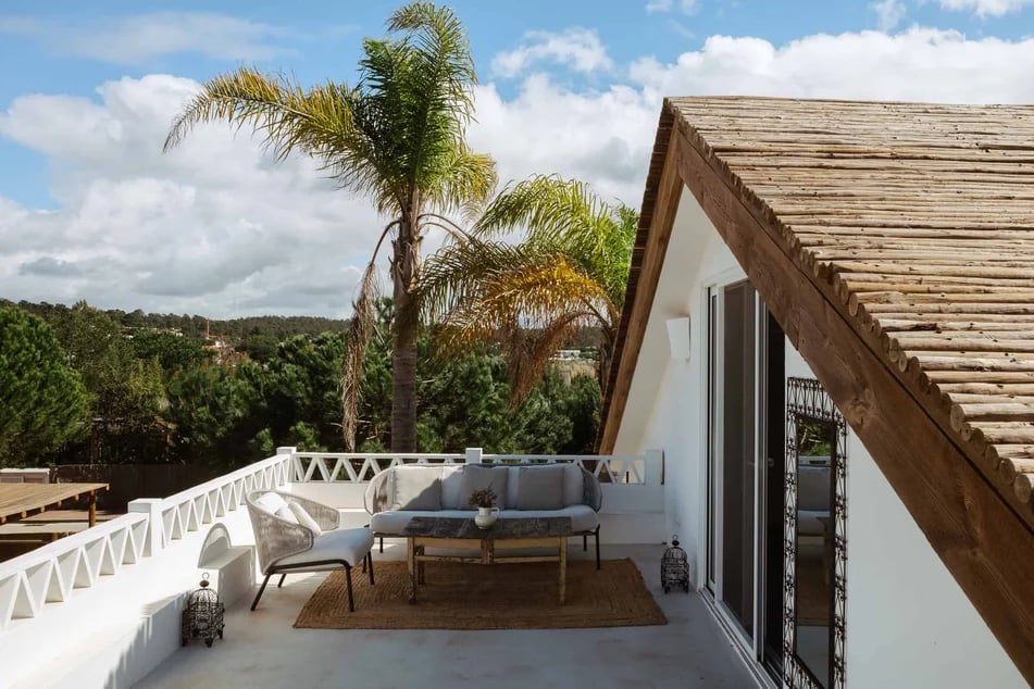 terrasse-avec-canapes-chaises-et-table-basse-d-une-maison-typique-blanche-avec-toit-en-bois-entouree-de-verdure