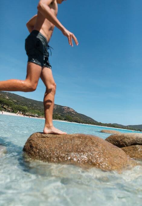 boy jumping from rock to rock in the water at beach in corsica boy jumping from rock to rock in the water at beach in corsica