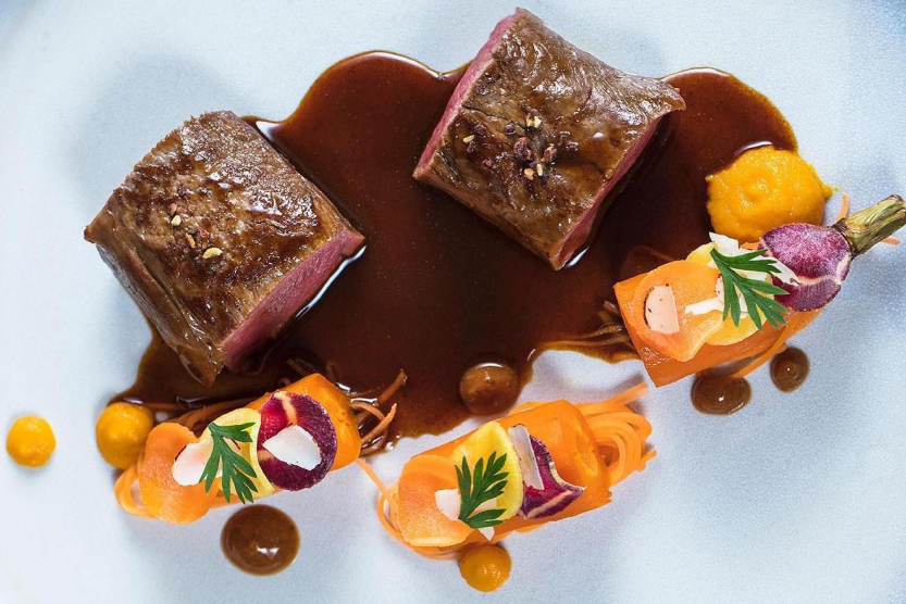 zoom-sur-une-assiette-gastronomique-avec-deux-morceaux-de-viande-trempant-dans-une-sauce-marron-et-une-carrotte-coupee-en-trois-autour