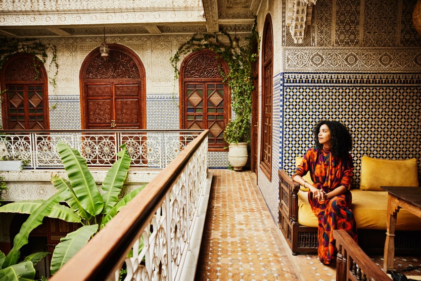 jeune-femme-en-tenue-coloree-admirant-les-plantes-a-l-etage-de-la-cour-interieure-d-un-riad-de-marrakech