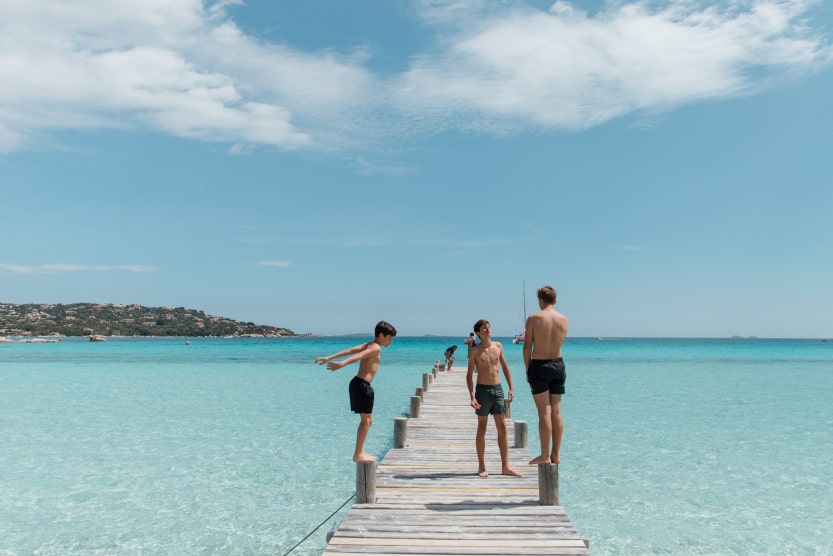 trois-freres-adolescents-debout-ensemble-sur-le-ponton-en-bois-d-une-plage-a-l-eau-turquoise-face-a-l-horizo-min