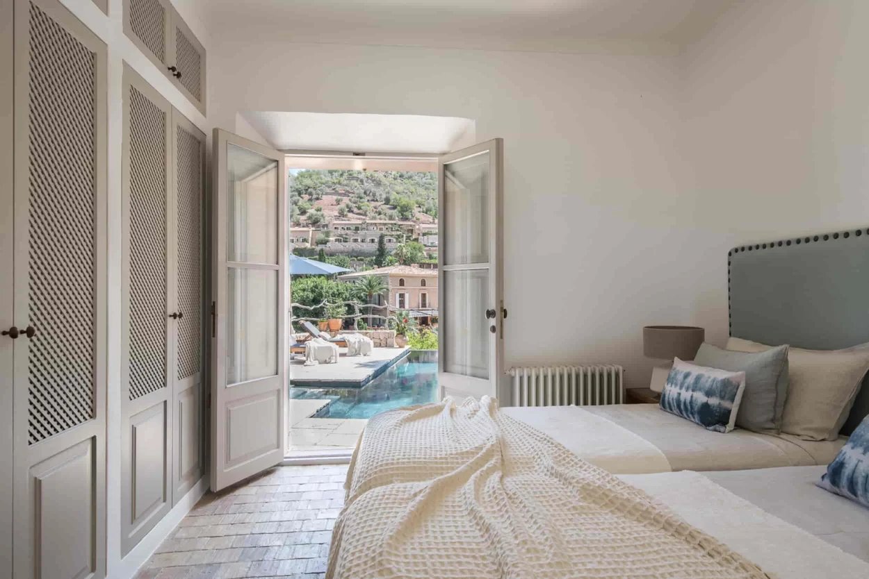 chambre-avec-deux-lits-simples-beiges-avec-coussins-beiges-gris-bleus-un-dressing-en-bois-blanc-et-des-portes-donnant-sur-la-piscine-avec-vue