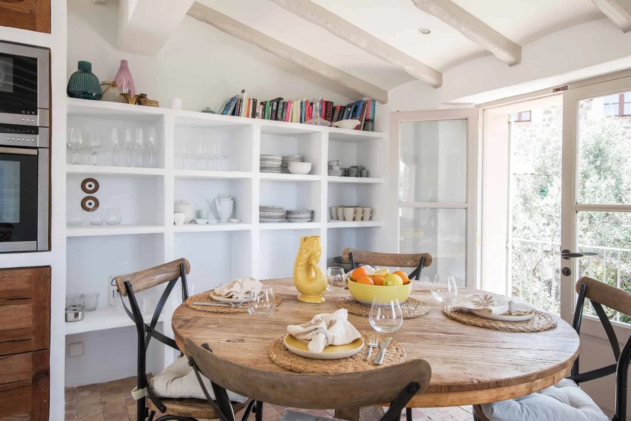 table-a-manger-en-bois-avec-quatre-chaises-en-bois-et-acier-noir-devant-une-etagere-blanche-avec-des-ustensiles-un-four-et-des-portes-fenetres