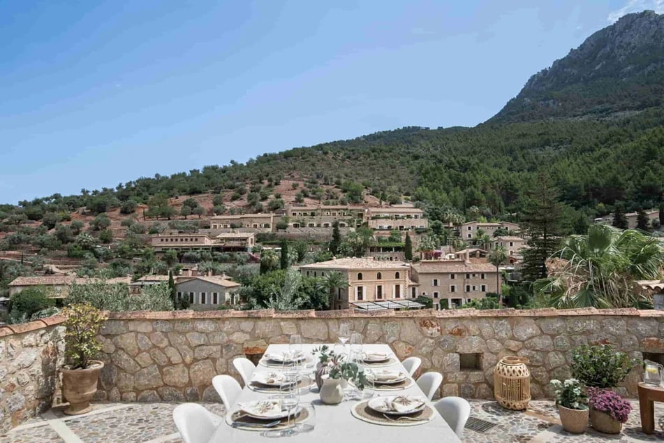 table-dresse-sur-une-terrasse-en-pierres-rempli-de-plantes-face-a-un-village-de-montagne-avec-des-maisons-en-pierres