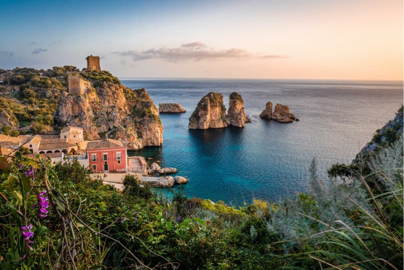 vue-depuis-une-colinne-sicilienne-verdoyante-sur-la-mer-et-une-petite-maison-traditionnelle-rouge-au-milieu-des-falaises-sous-le-coucher-du-soleil