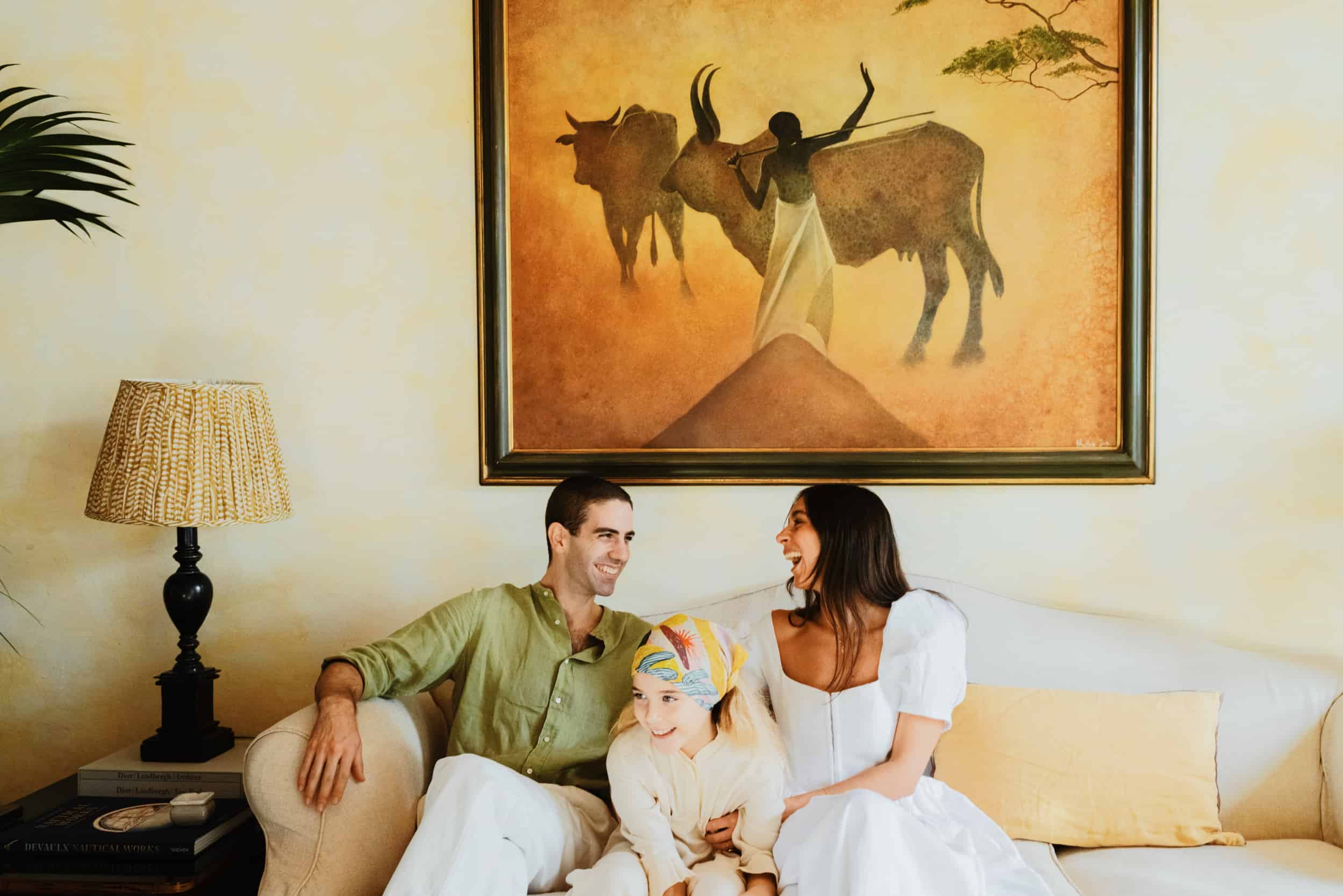 Woman-in-white-dress-and-man-in-green-shirt-sat-on-a-couch-with-a-little-girl-all laughing