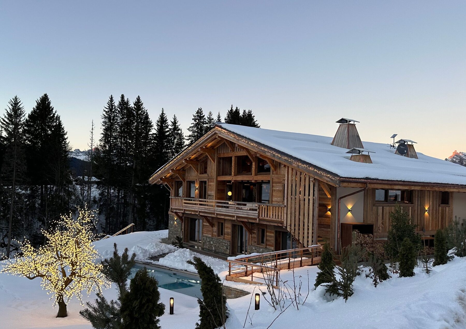Le Chalet Vantage à Megève sous la neige, illuminé au crépuscule au bord de sa piscine chauffée
