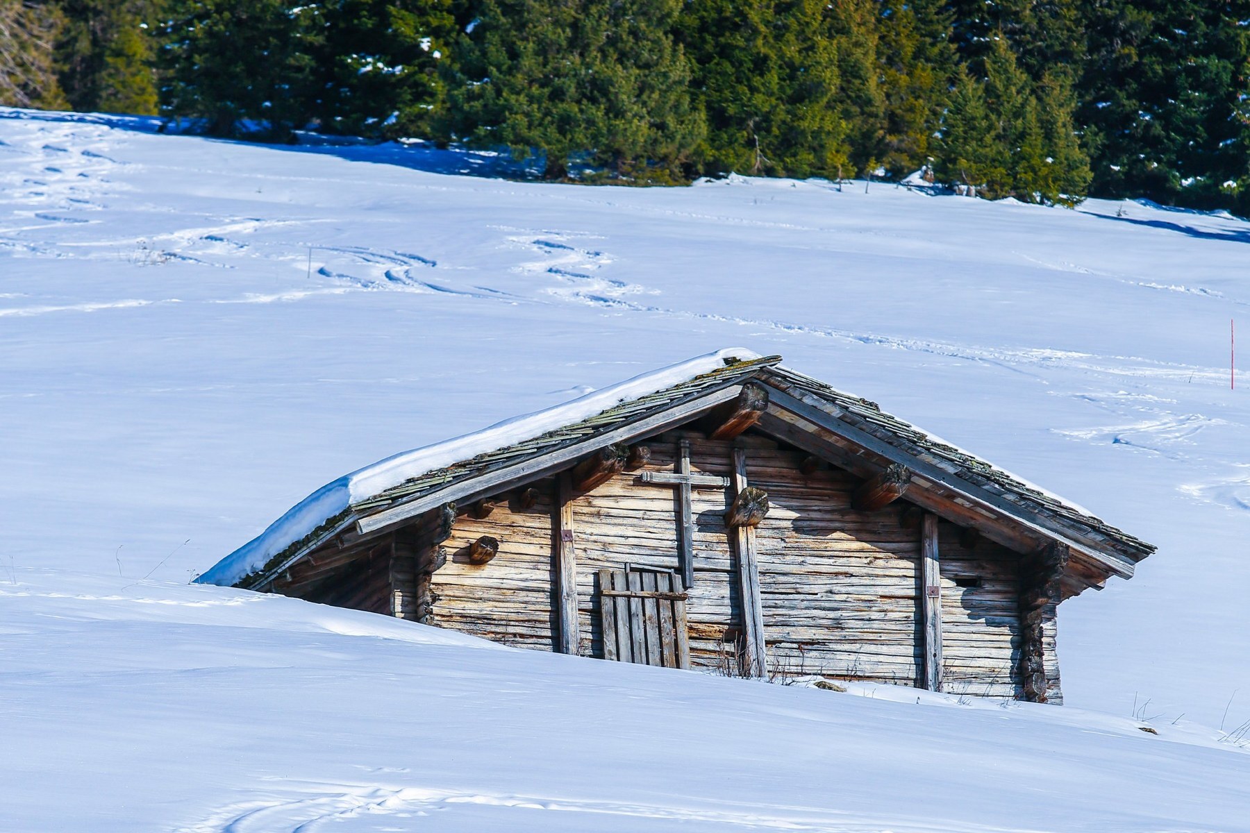 Un chalet de bois enfoui sous la neige au milieu des pistes