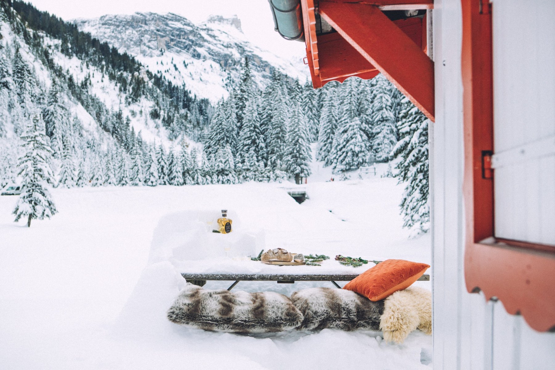 Une table de bois dressée dans la neige devant un chalet, face aux montagnes