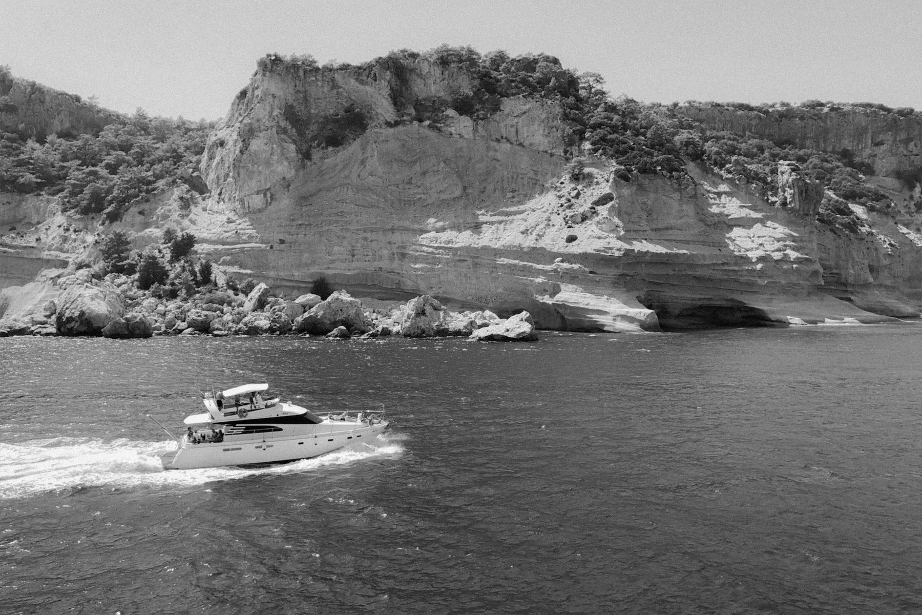Un bateau privé longe des falaises calcaires, en noir et blanc